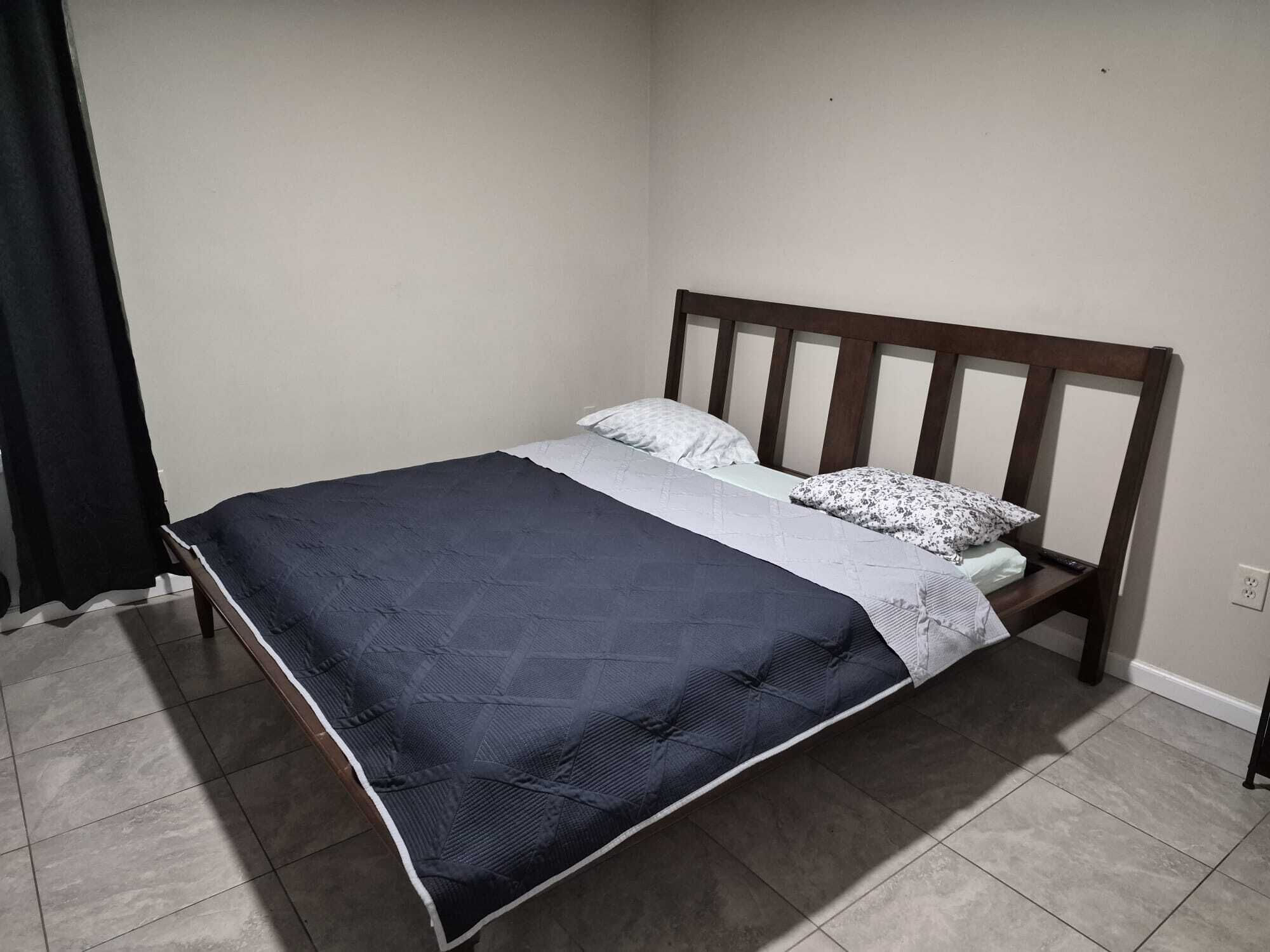 A single bed with a wooden headboard, a dark blue quilt, and a white pillow.