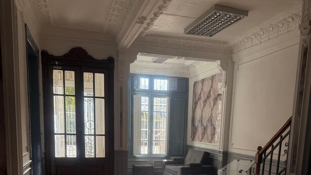 Un pasillo amplio con suelo de madera, baranda de cristal y vista a una puerta con paneles de vidrio.