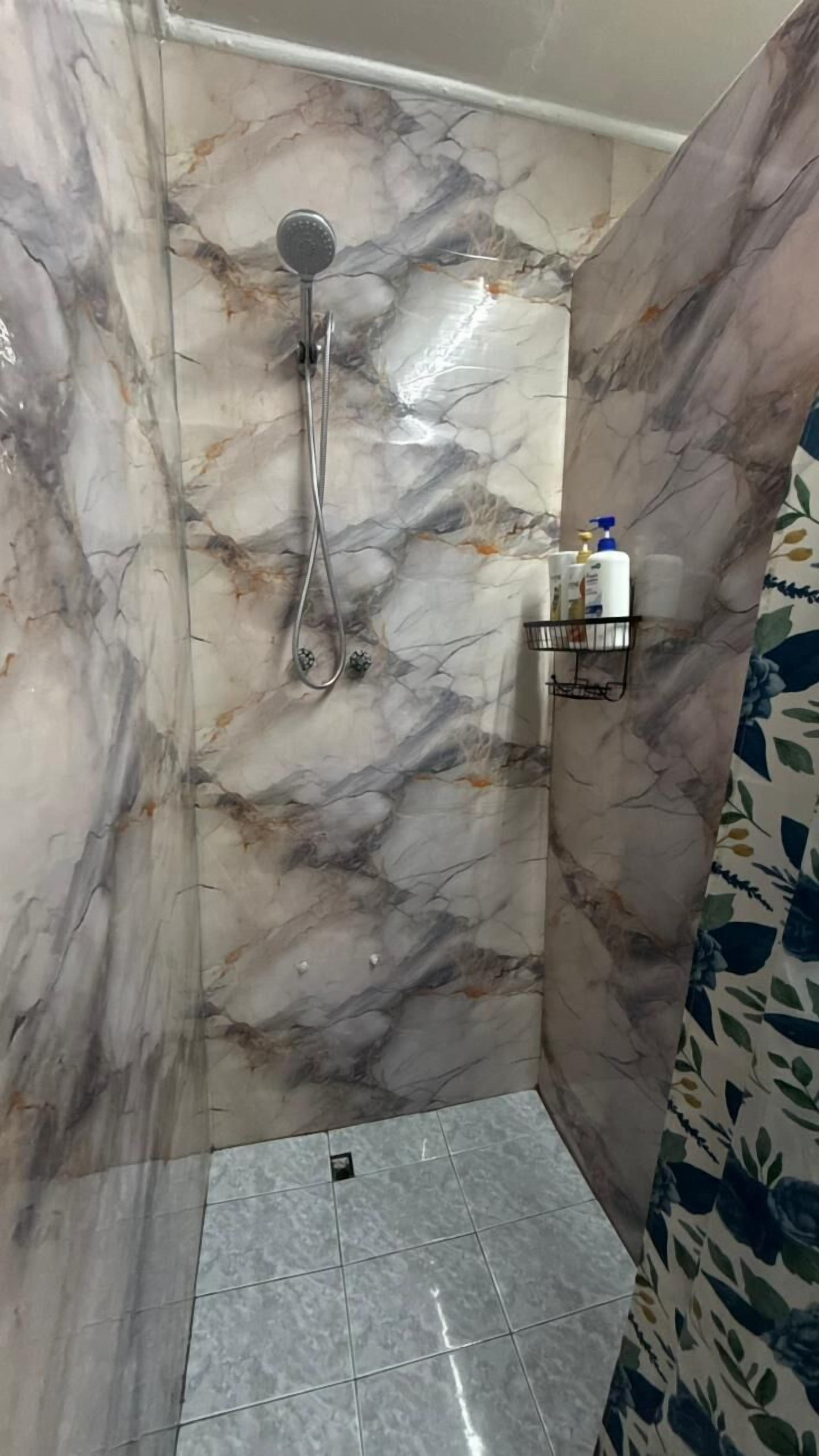 A small, tiled shower area with a marble wall and a showerhead.