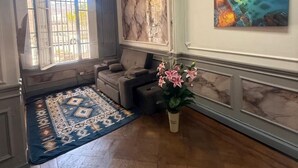 Una habitación con un ventanal grande, un cuadro de una escena costera, un tapete estampado y un sofá.