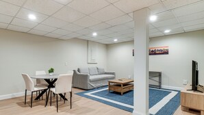Uma sala de estar moderna com área de jantar, um sofá cinza, uma mesa de centro e um rack para TV.