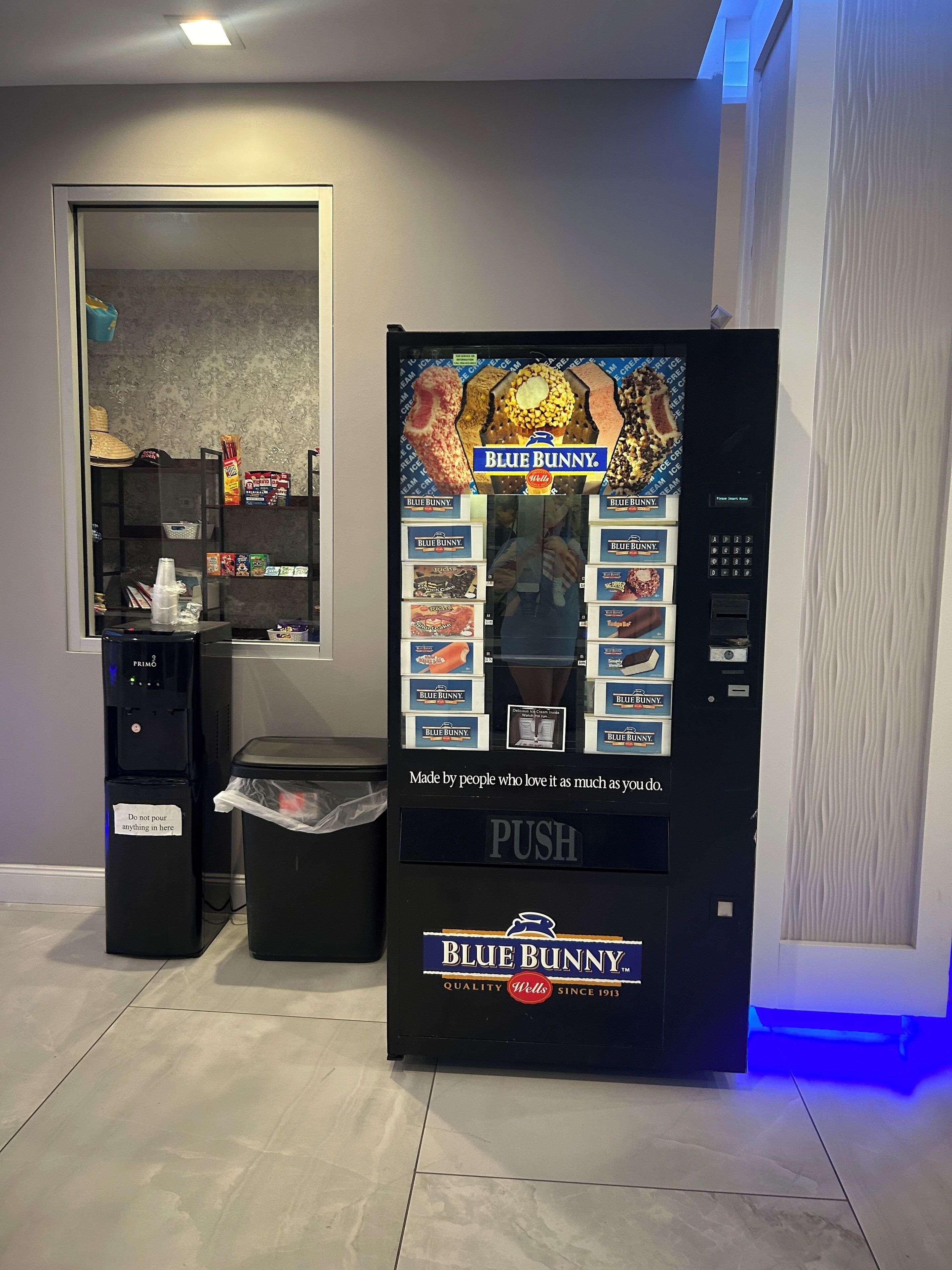 Un distributeur automatique de la marque Blue Bunny, avec un point d’eau et une poubelle à proximité.