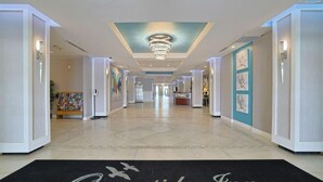 Un vaste couloir d’hôtel doté d’un plafond au design moderne, d’un comptoir de réception et d’œuvres d’art encadrées accrochées aux murs.