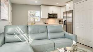 A modern living room with a light blue leather sofa, a glass coffee table, and a kitchen area with white cabinets and stainless steel appliances. - 4 Mi to Downtown Tampa! Urban Couples Retreat (Tampa)
