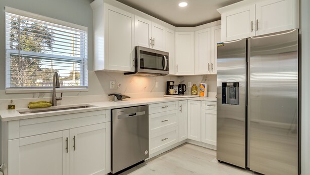 A modern kitchen with white cabinets, stainless steel appliances, a dishwasher, and a window with blinds. - 4 Mi to Downtown Tampa! Urban Couples Retreat (Tampa)