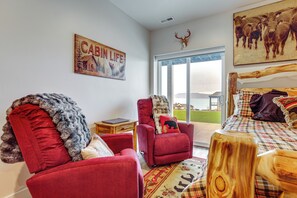 A cabin-themed room with a red armchair, a wooden headboard bed, and a large window with a view of the outdoors. - Hot Tub & Pickleball Court: Huge Bear Lake Home! (Garden City)