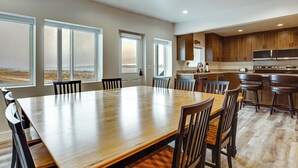 Un comedor amplio con una gran mesa de madera y sillas, una cocina con armarios de madera y electrodomésticos de acero inoxidable, y grandes ventanales con vistas al paisaje.
