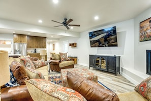 A spacious living room with a large brown leather sofa, a wooden coffee table, and a television mounted on the wall. - Hot Tub & Pickleball Court: Huge Bear Lake Home! (Garden City)