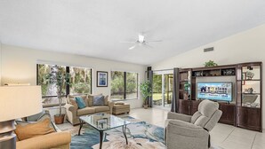 A spacious living room with a glass coffee table, two sofas, a recliner, a ceiling fan, and a TV on a wooden cabinet. - Tranquil Sarasota Retreat Near Beaches, Pool & Nature Escape - Timberwood Villa #183 - Roelens (Sarasota)