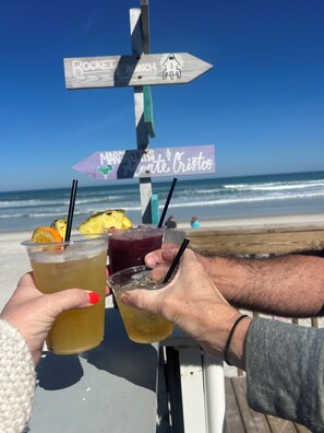 A beachside bar with drinks and a signpost with directions. - Perfect location - Seconds to toes in the sand or oceanfront pool (Daytona Beach)