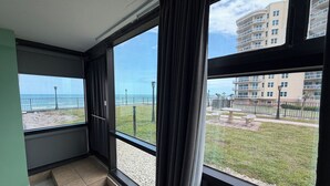 A room with large windows, a view of the beach, and a building in the background. - Oceanview King Studio - Outside Terrace, Beachfront Pool & Tiki (Daytona Beach)