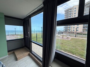 Een kamer met grote ramen, uitzicht op het strand en een gebouw op de achtergrond.