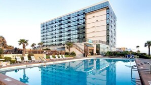 A modern hotel with a large pool, palm trees, and a clear sky. - Oceanview King Studio - Outside Terrace, Beachfront Pool & Tiki (Daytona Beach)