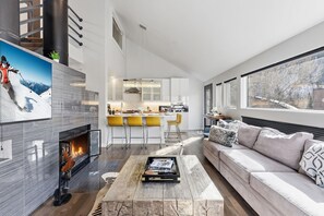 A modern living room with a fireplace, a sofa, a coffee table, and a kitchen in the background. - East Vail Escape - Mountain Views & Shared Hot Tub (Vail)