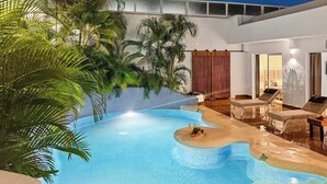 Una piscina interior de borde curvo, rodeada de sillones de descanso y plantas en macetas.