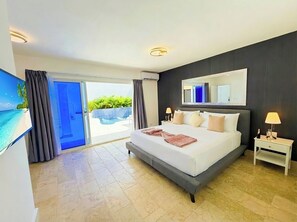 Ein modernes Hotelzimmer mit einem großen Bett, einem Fernseher, einer Schiebetür zu einem Poolbereich und einer dunkel gefärbten Wand.