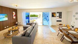 Una sala de estar moderna con un sofá, una mesa de comedor lista para el desayuno y un televisor montado en la pared.