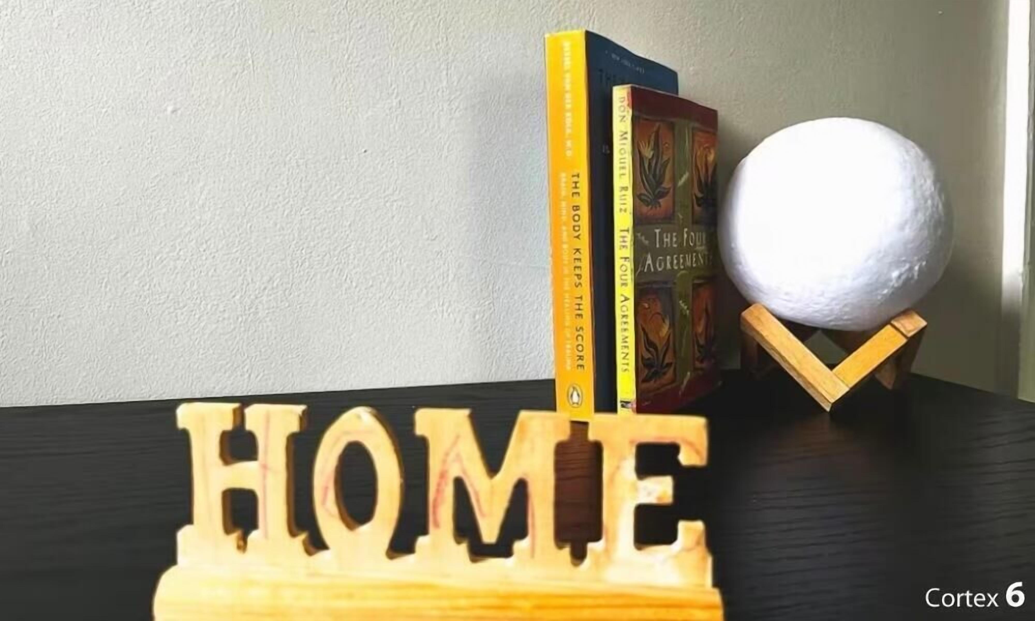 A wooden block with the word "HOME" and two books titled "The Body Keeps the Score" and "The Four Agreements" on a dark surface.