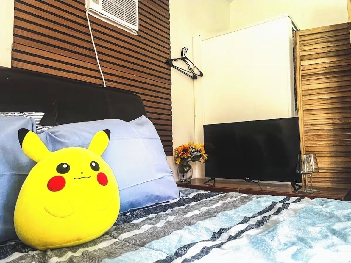 A bed with a striped blanket, a Pikachu plush toy, a vase with flowers, a TV, and a wooden wall.