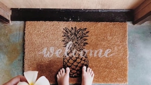 Un paillasson à motifs d’ananas, avec le mot « bienvenue » inscrit dessus, le tout sur un fond marron.