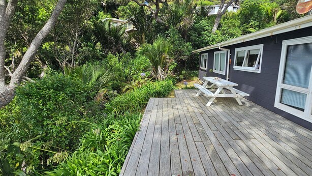 A wooden deck with a picnic table, surrounded by dense greenery and trees. - Beachfront Property in Private Bay with only 12 houses and private beach access. (Matapouri)