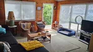 A cozy cabin interior with a dark sofa, wicker chairs, a small table, and a television. - Beachfront Property in Private Bay with only 12 houses and private beach access. (Matapouri)
