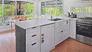 Une cuisine moderne dotée d’un grand îlot central, d’appareils électroménagers en acier inoxydable et de grandes fenêtres offrant une vue sur la verdure.