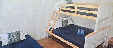 Une chambre avec deux lits superposés, dont l’un est muni d’une échelle en bois, et une petite table.