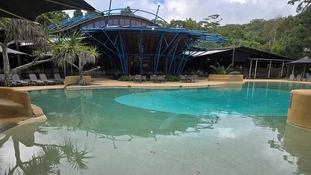 Une piscine avec des chaises longues et un espace abrité doté d’un toit bleu.