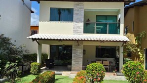 Una casa de dos pisos con un porche cubierto, un pequeño jardín con flores y un cielo despejado.