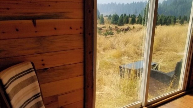 L’intérieur d’un chalet en bois, avec une grande fenêtre donnant sur un champ verdoyant et des arbres au loin.