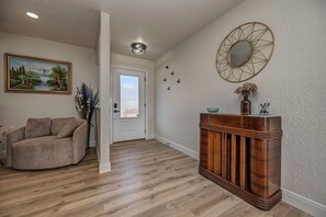 A living room with a beige sofa, wooden flooring, a painting, a decorative mirror, and a vase with dried flowers.