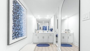 Een moderne badkamer met witte kasten, een grote spiegel en een blauw abstract schilderij.