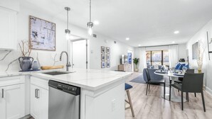 Een moderne keuken met een vaatwasser, een eethoek met tafel en stoelen, en een groot raam dat zorgt voor natuurlijk licht.