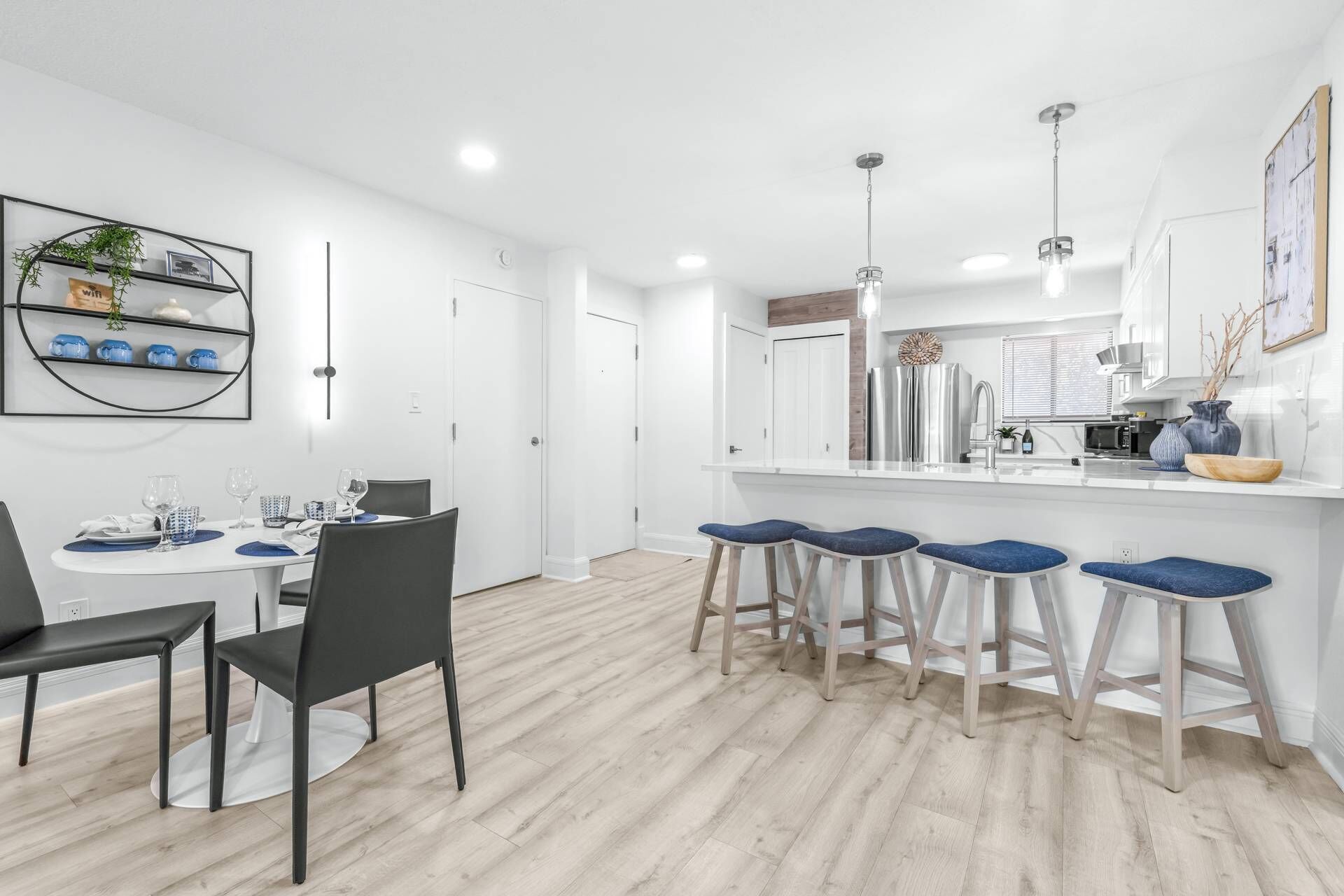 Een moderne keuken met een centraal eiland, barkrukken en een zithoek met stoelen en een tafel.