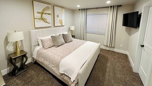 Un dormitorio con cama, mesitas de noche, televisor y cuadros en la pared.