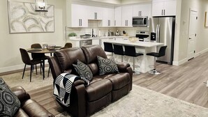 Una cocina moderna con armarios blancos, electrodomésticos de acero inoxidable y una zona de comedor con sofá y sillones de cuero.