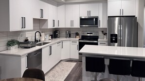 Una cocina moderna con armarios blancos, electrodomésticos de acero inoxidable y una barra con taburetes.