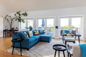 A modern living room with a blue sectional sofa, a small black coffee table, and a large window offering a view of the outdoors. - Hummingway Ranch, by Vinifera Homes (Forestville)
