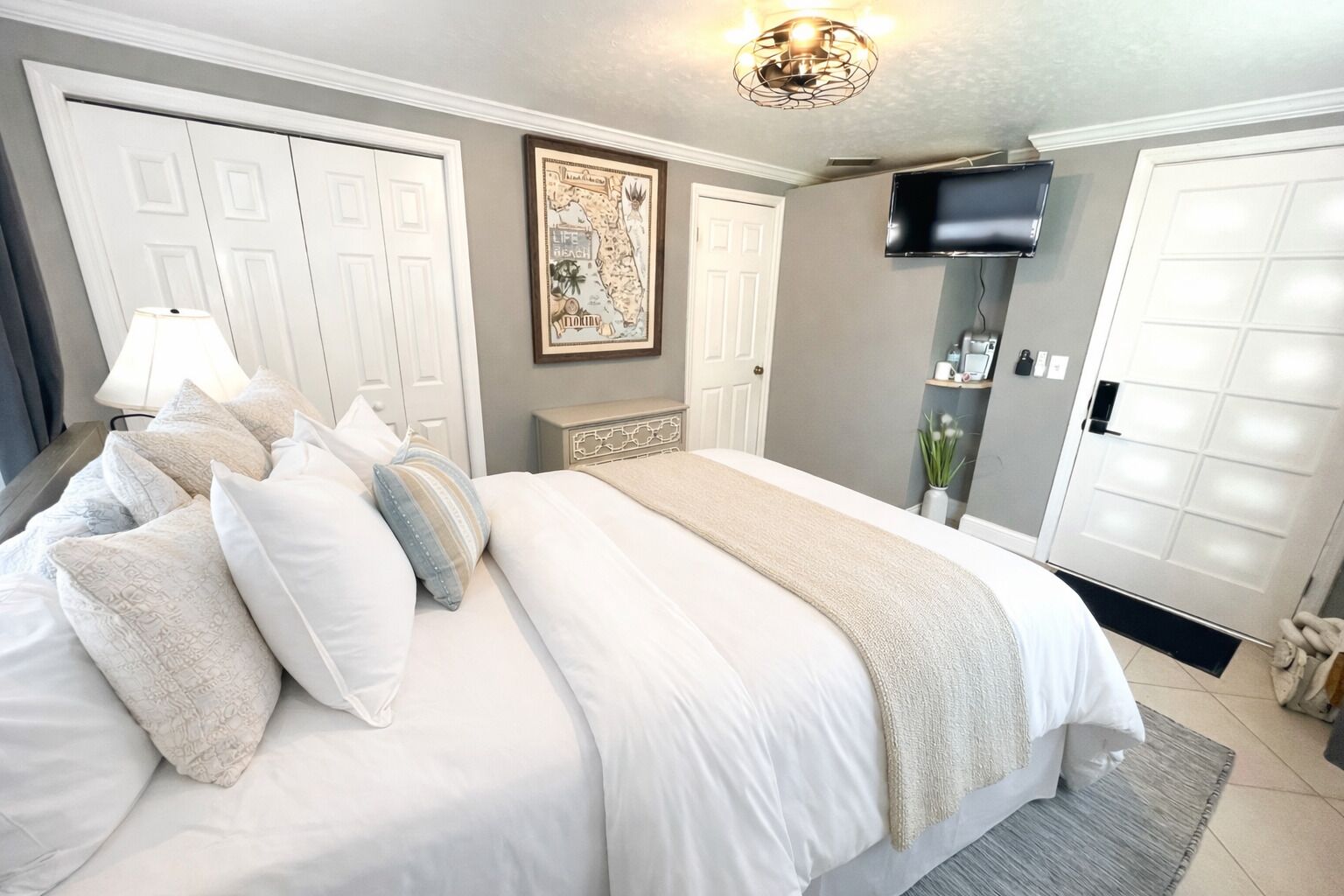 A bedroom with a large bed, white walls, a mounted TV, and a framed map on the wall.