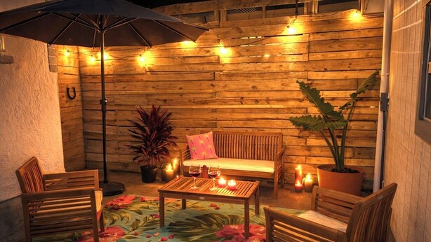 Un patio al aire libre con muebles de madera, alfombra floral e iluminación colgante.