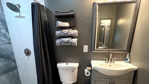 Un baño con ducha, inodoro, lavamanos y espejo con iluminación.