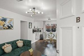 Una sala de estar moderna con un sofá verde, una mesa de comedor con sillas y una cocina al fondo.