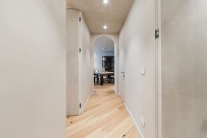 A narrow hallway with wooden flooring and white walls, leading to a dining area with a table and chairs. - Lakeside Luxe Apartment 2BR Prime Location (Tirana)