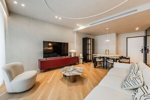 A modern living room with a flat-screen TV, a red console table, a marble coffee table, a sofa with patterned cushions, and a dining area with a table and chairs. - Lakeside Luxe Apartment 2BR Prime Location (Tirana)