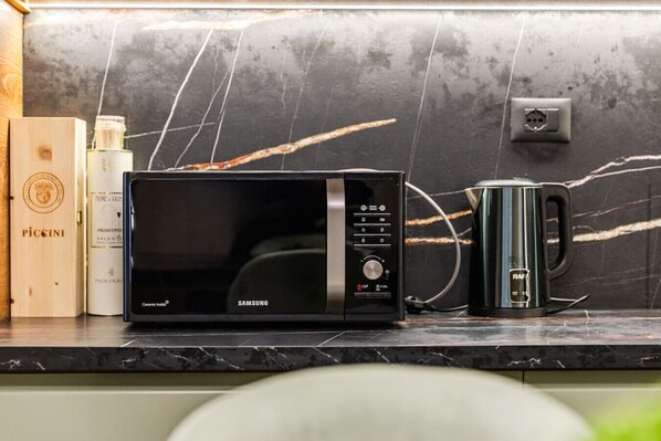 A kitchen with a black microwave, a black coffee maker, and a wooden box with a logo. - Miracle No 8 Central Modern Duplex (Tirana)