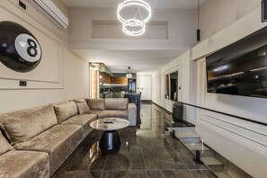 Un salon moderne avec un canapé d’angle, une table basse ronde et un grand téléviseur.