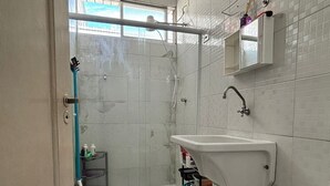 Een badkamer met douche, wastafel, toilet en een klein raam.