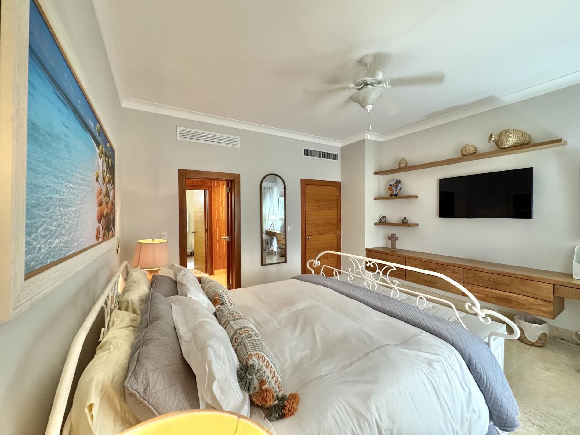 Un dormitorio con cama, ventilador de techo, televisor y un cuadro en la pared.