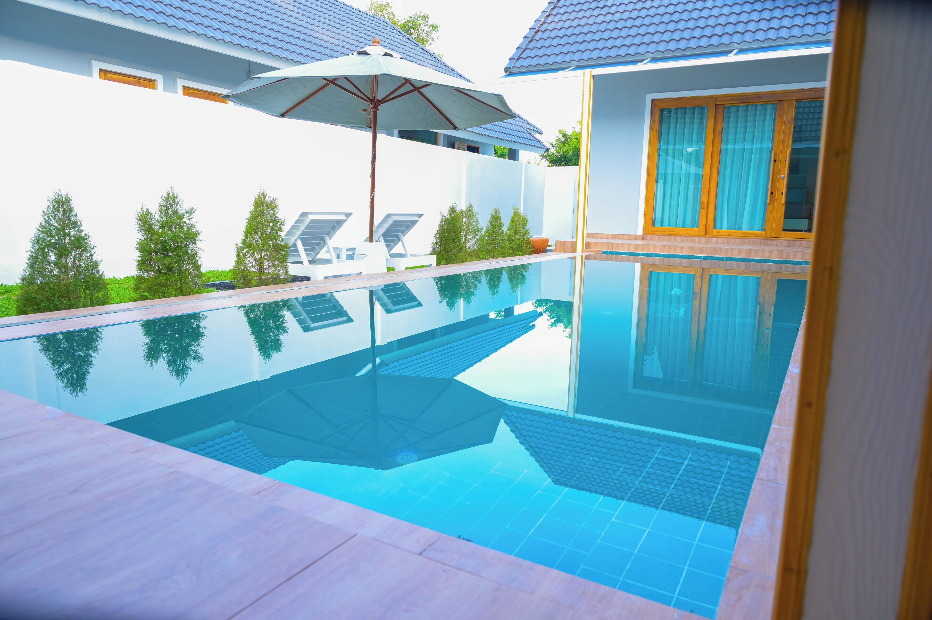 A modern swimming pool with clear blue water, surrounded by a tiled deck and a white building with a blue roof.